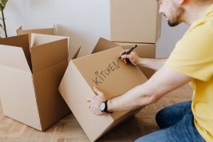 Man writing kitchen on moving box