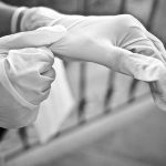 Two hands putting on white gloves